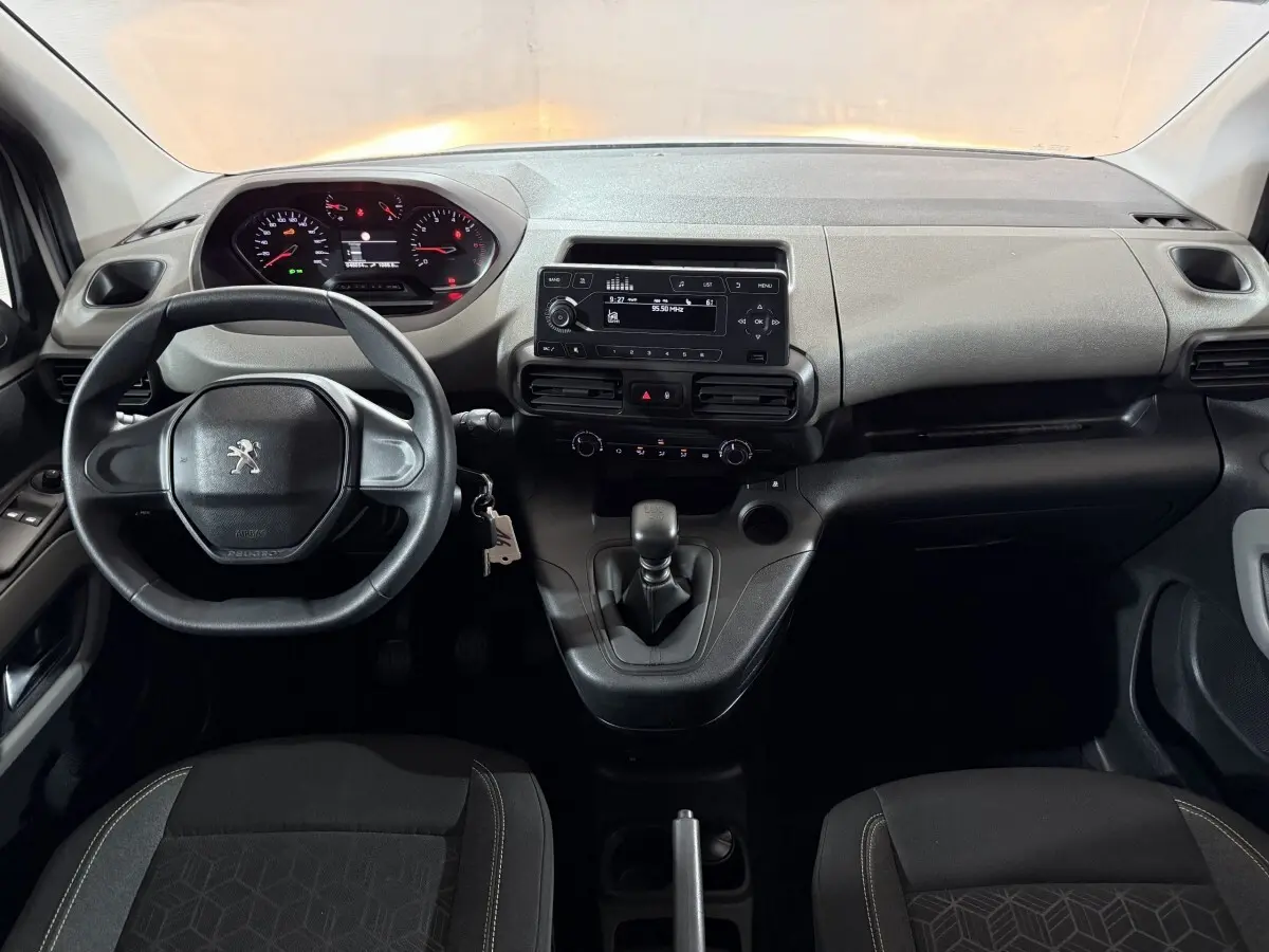 Vue intérieure frontale du tableau de bord noir et gris du Peugeot Rifter avec volant, écran central et levier de vitesses manuel.