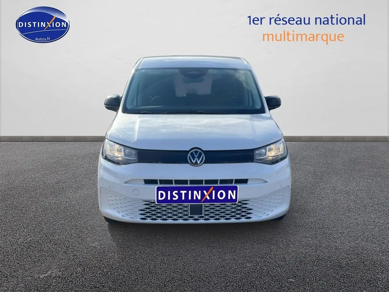 Vue frontale d'un Volkswagen Caddy blanc 2025 avec calandre noire et plaque Distinxion visible.