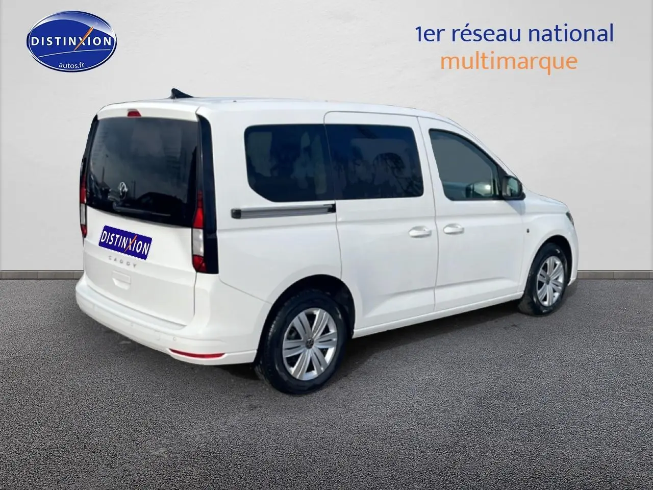 Volkswagen Caddy blanc vue 3/4 arrière droit avec vitres teintées et jantes alliage.