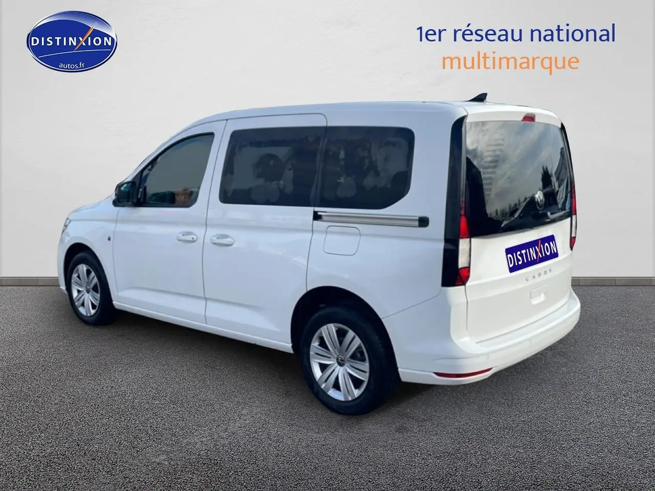 Vue 3/4 arrière droite du Volkswagen Caddy blanc 2025 avec vitres arrière teintées et barres de toit noires.