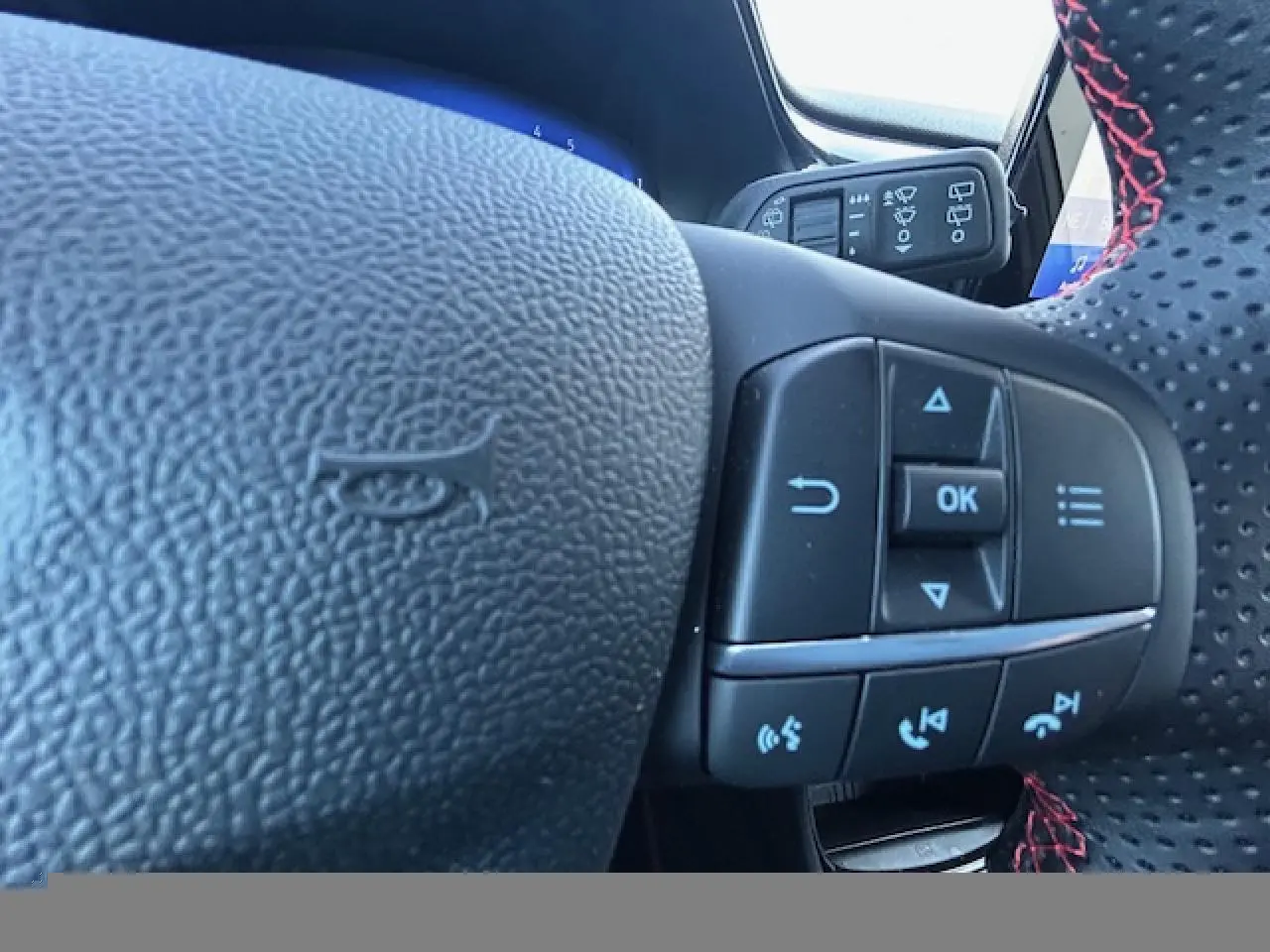 Gros plan sur le volant perforé avec surpiqûres rouges et commandes multifonctions du Ford Puma gris Solar 2023.