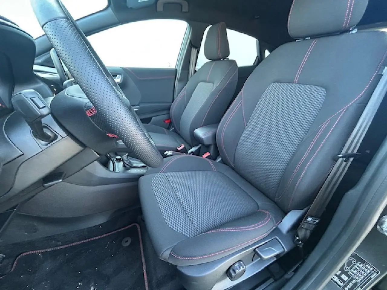 Vue intérieure côté conducteur du Ford Puma gris Solar 2023, sièges noirs avec surpiqûres rouges et volant perforé ST-Line.