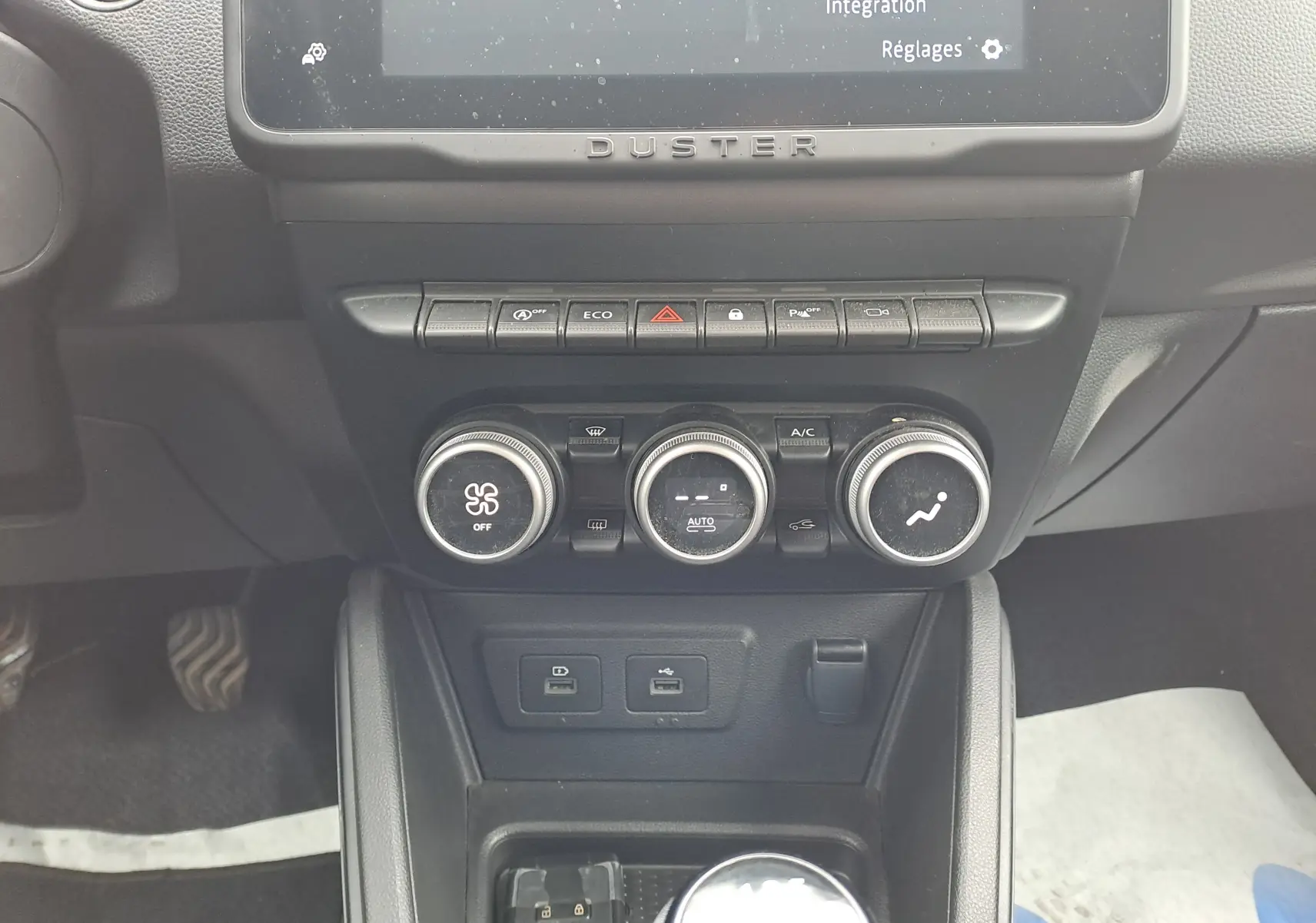 Vue rapprochée du tableau de bord central du Dacia Duster 2024, avec commandes de climatisation et écran tactile.
