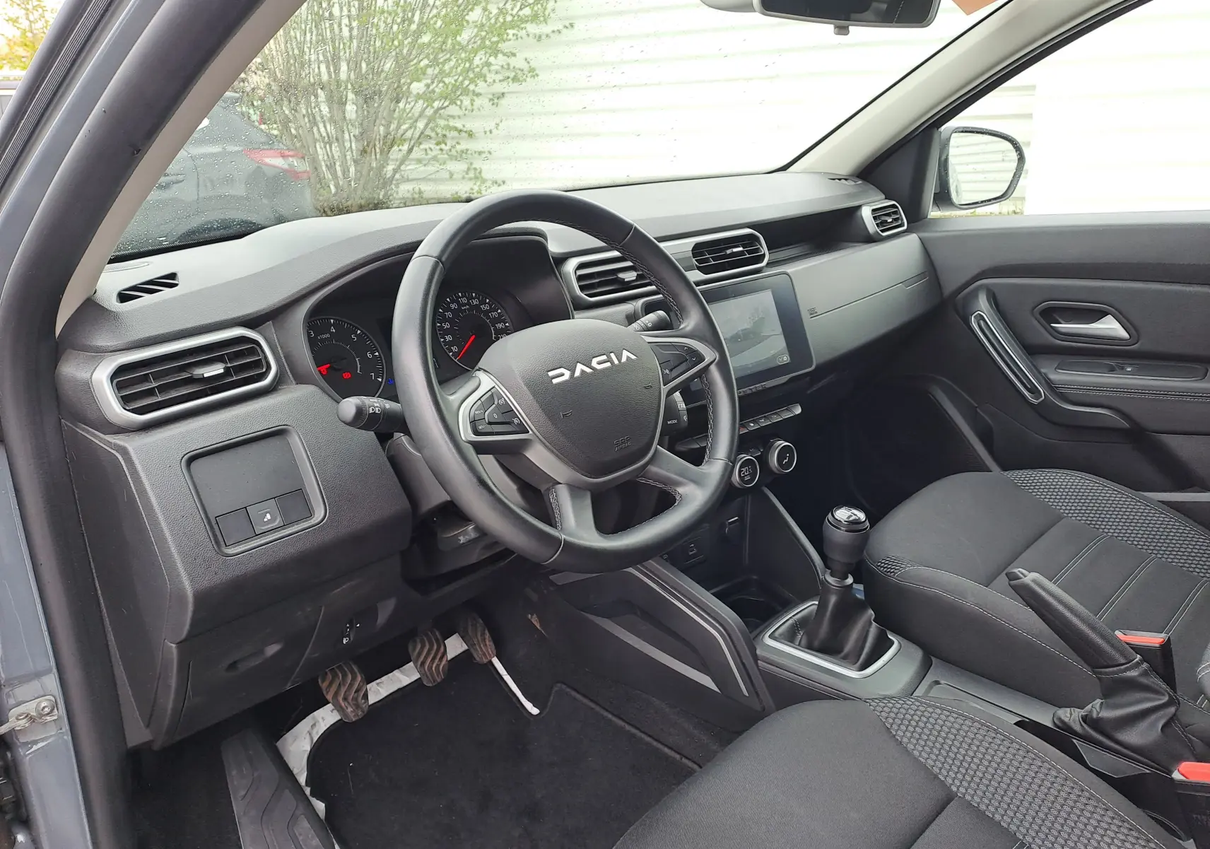 Vue intérieure côté conducteur du Dacia Duster 2024 gris urbain, volant multifonction et boîte manuelle visibles.