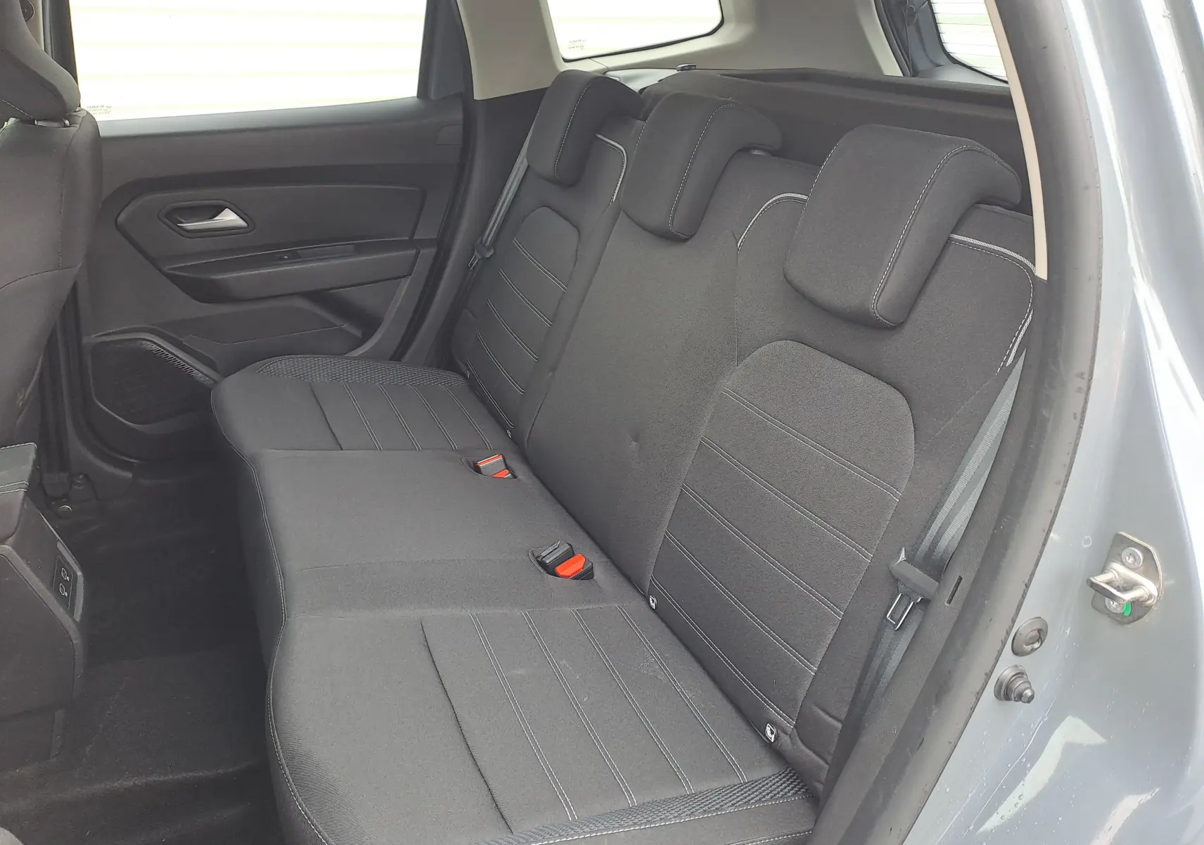 Vue intérieure côté arrière droit du Dacia Duster gris urbain 2024, montrant la banquette arrière noire avec appuie-têtes intégrés.