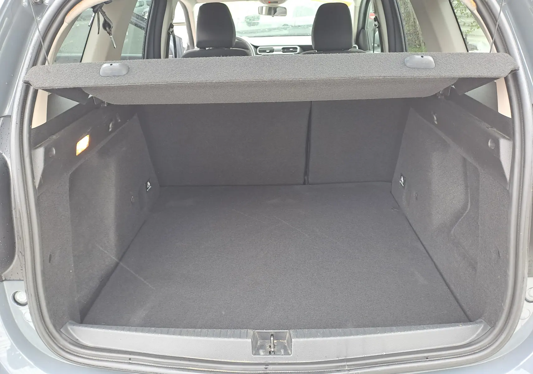 Vue du coffre ouvert d'un Dacia Duster gris urbain 2024, montrant l'espace de chargement avec cache-bagages déployé.