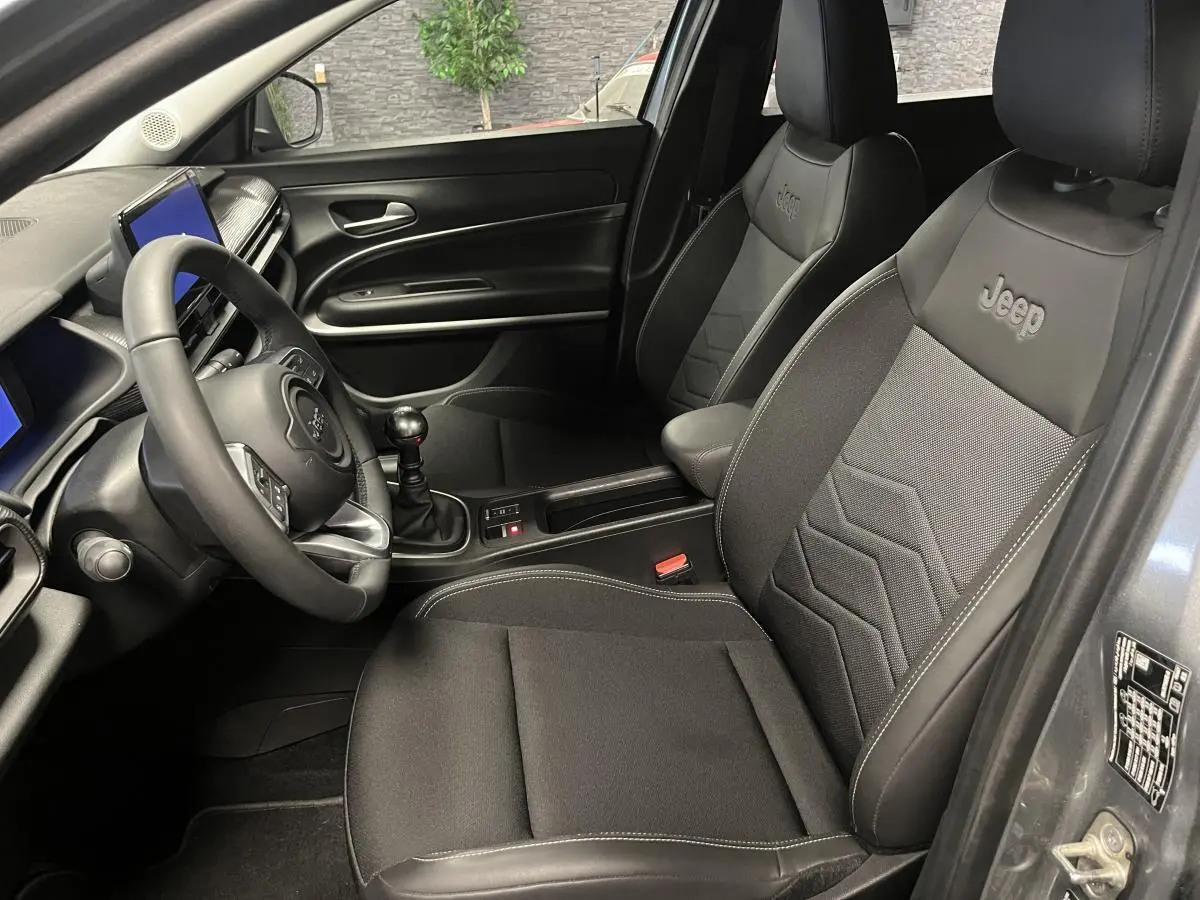 Vue intérieure côté conducteur du Jeep Avenger gris, mettant en valeur les sièges noirs avec logo Jeep brodé.