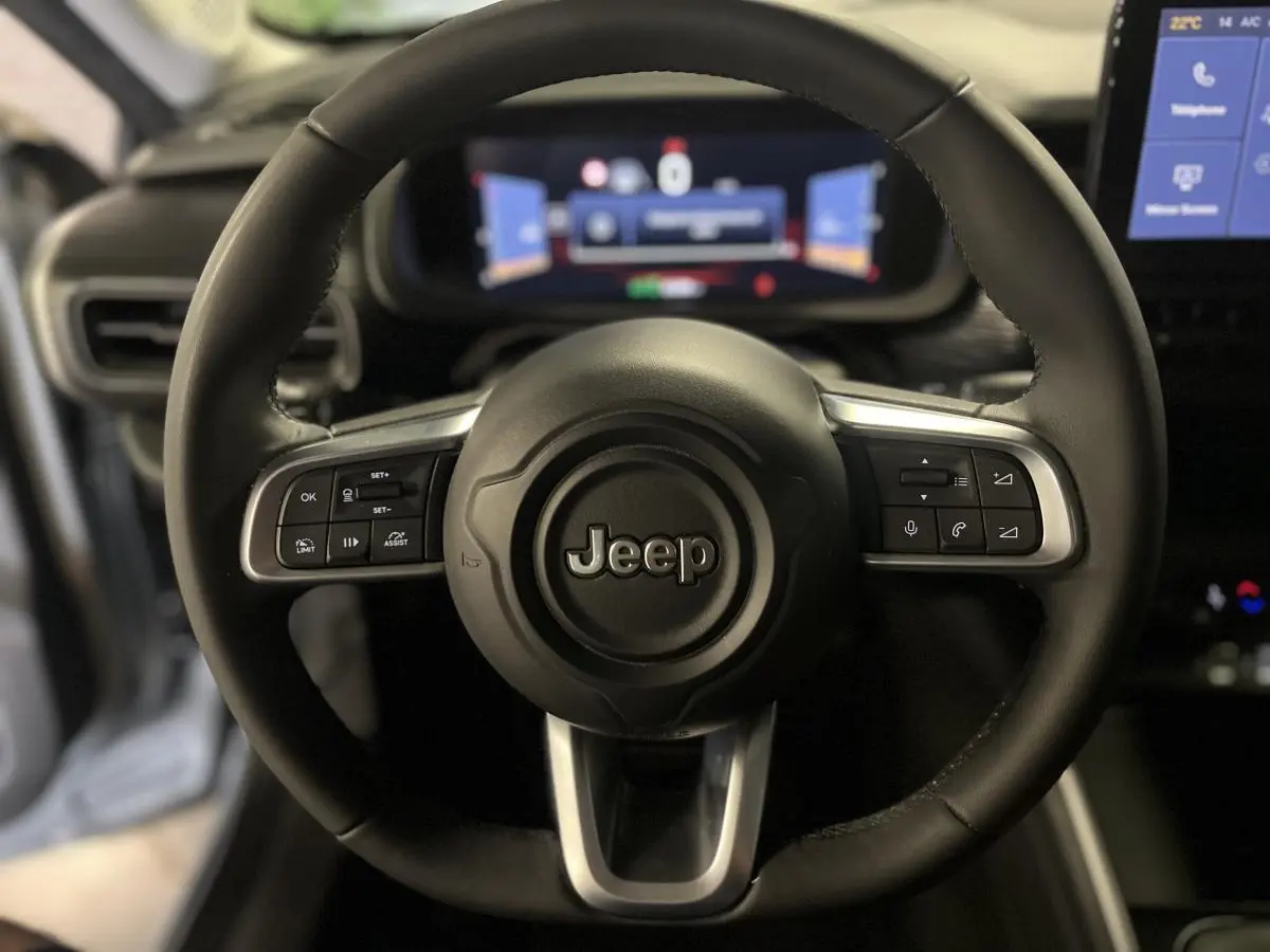 Vue rapprochée du volant en TEP noir du Jeep Avenger 2024 avec commandes intégrées et tableau de bord numérique flou.
