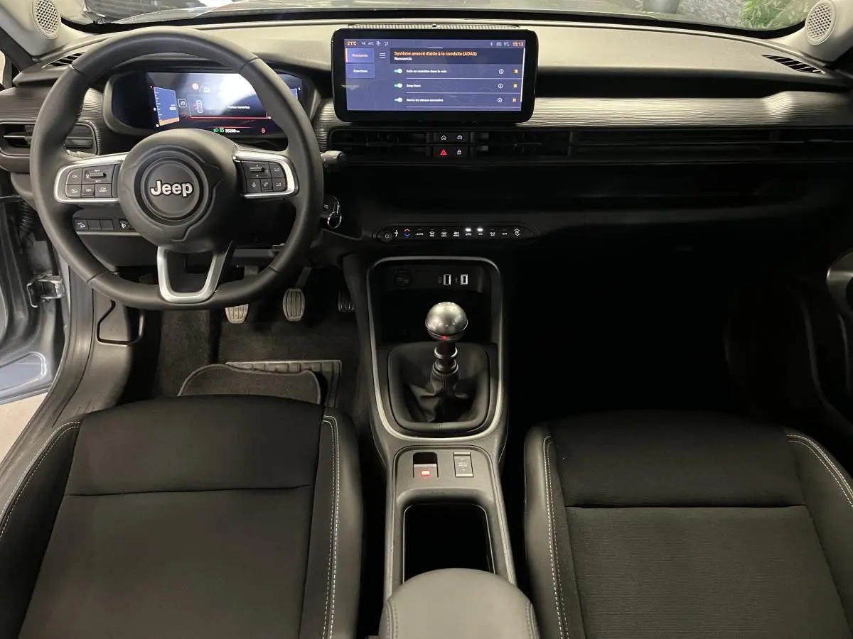 Vue intérieure frontale du tableau de bord et console centrale du Jeep Avenger 2024, volant Jeep et écran tactile visible.