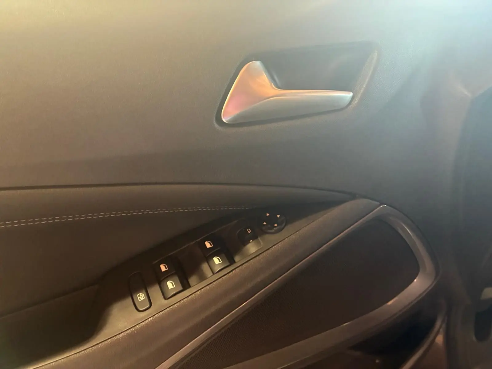 Gros plan sur la porte intérieure côté conducteur de l’Opel Crossland gris, montrant les commandes des vitres et la poignée argentée.