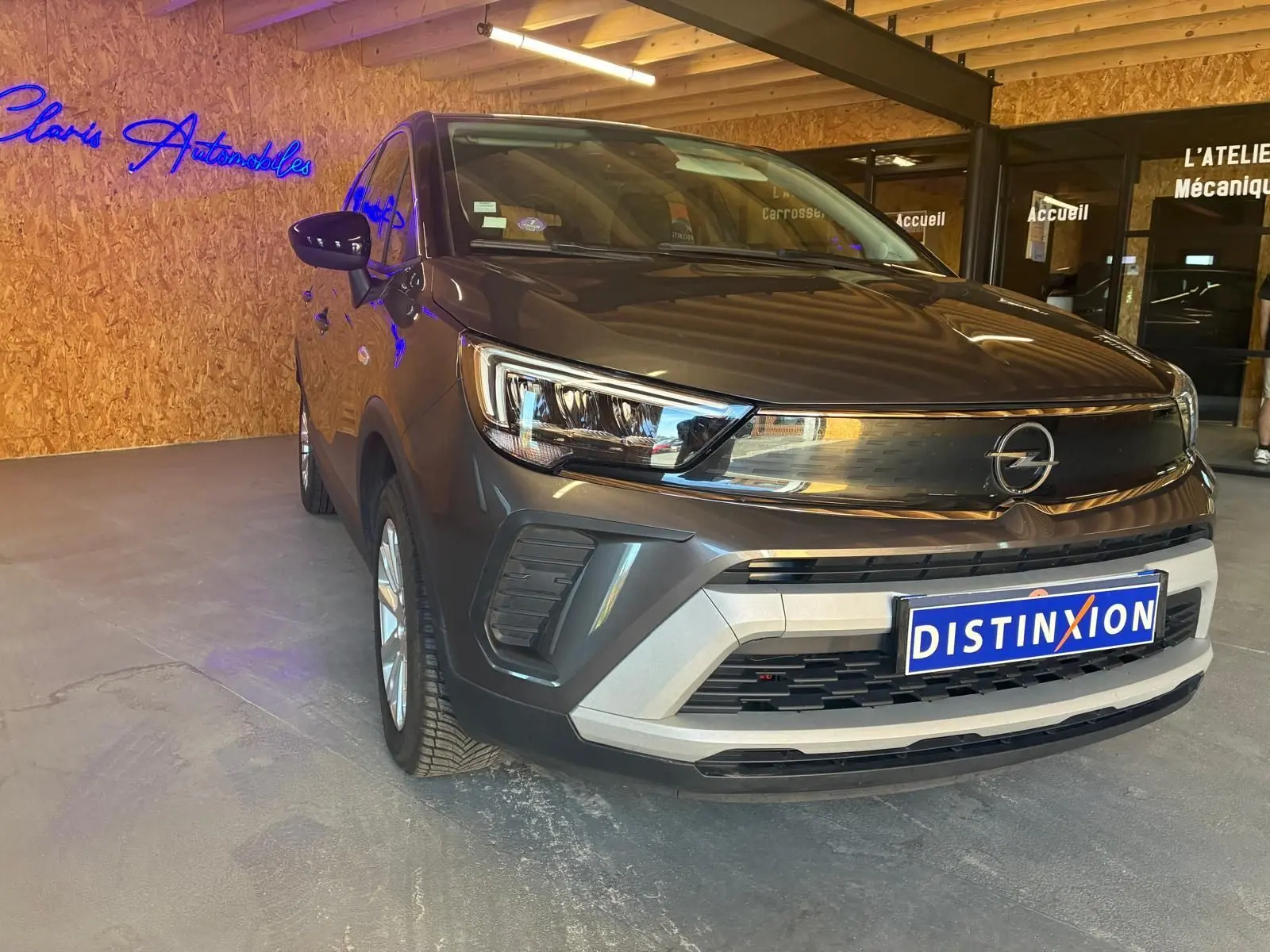 Opel Crossland gris en 3/4 avant droit, avec calandre noire brillante et plaque Distinxion visible.