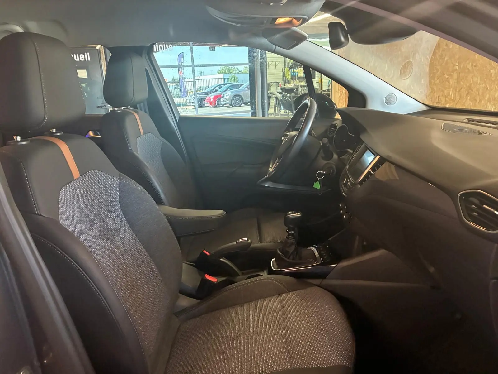 Vue intérieure côté gauche de l’Opel Crossland gris 2021, montrant les sièges tissu gris-noir et la console centrale avec boîte manuelle.