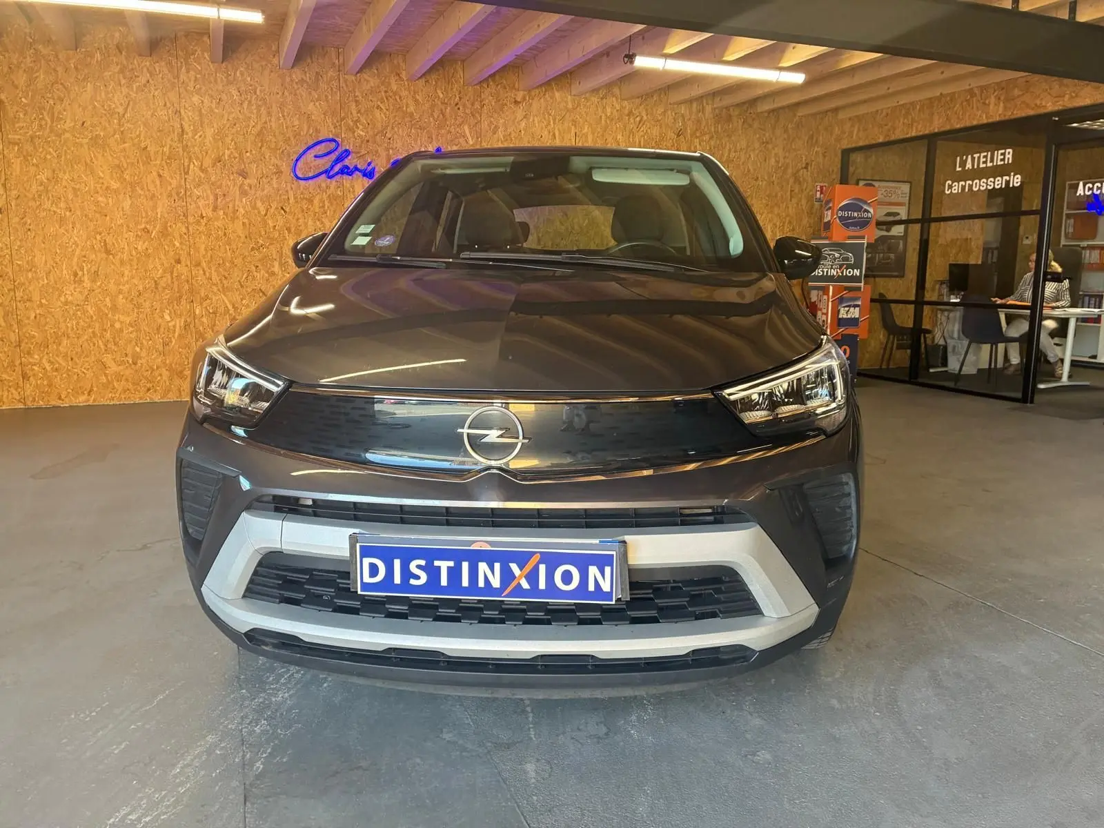 Vue frontale d’un Opel Crossland gris 2021 dans un showroom avec logo Opel et plaque Distinxion visible.