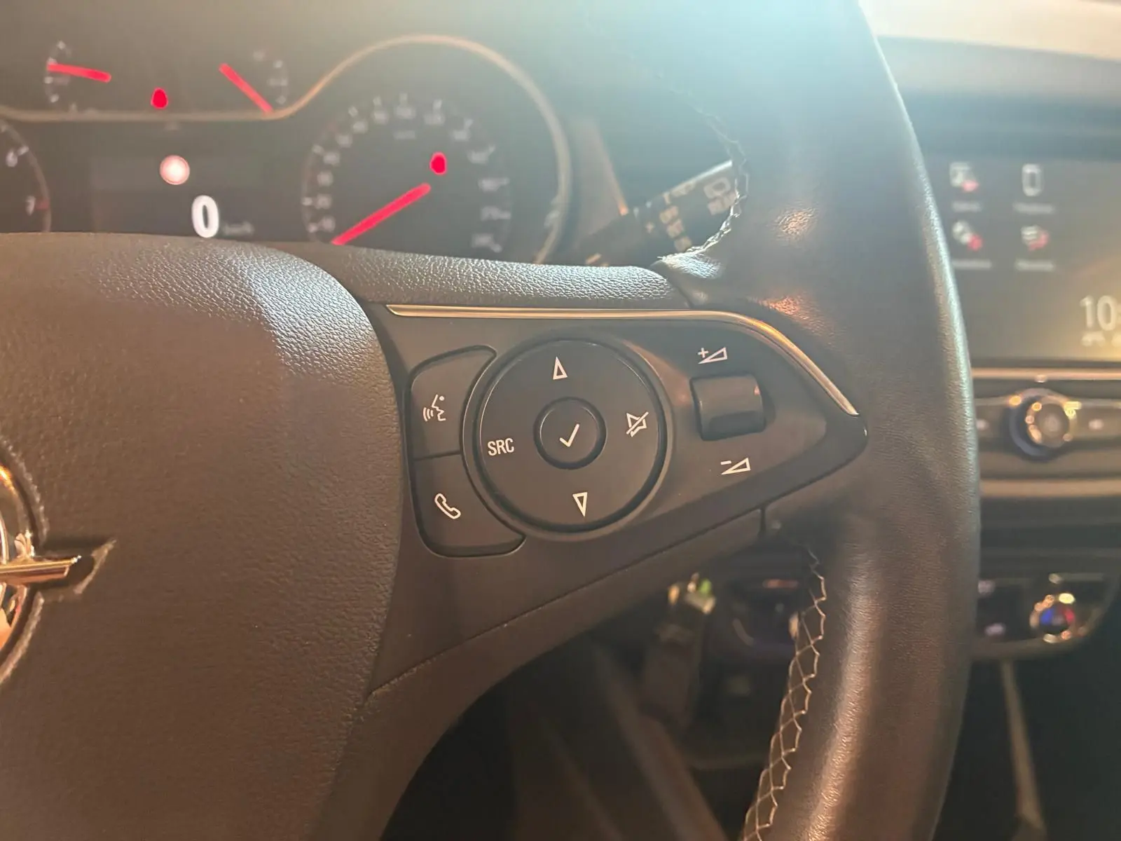Gros plan sur les commandes au volant à droite d'un Opel Crossland gris, avec tableau de bord et écran central en arrière-plan flou.