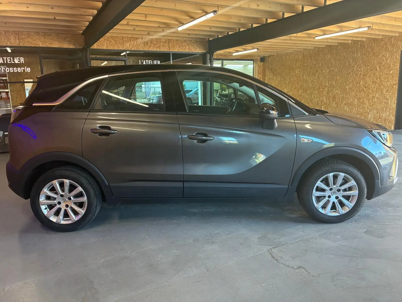 Vue de profil côté gauche d’un Opel Crossland gris 2021 avec jantes alliage et toit noir dans un garage.