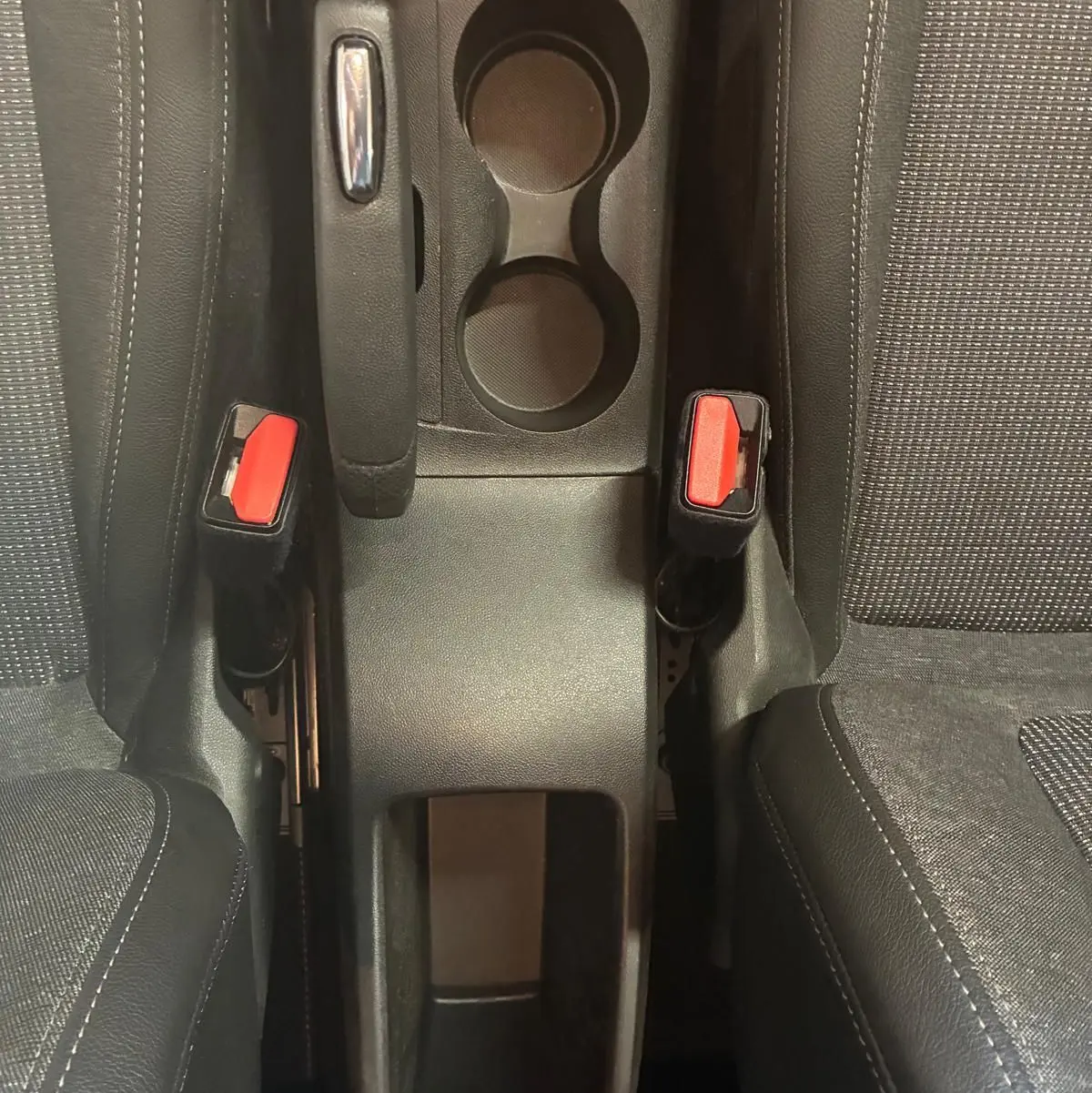 Vue plongeante sur la console centrale grise de l'Opel Crossland 2021, avec frein à main et porte-gobelets entre sièges tissu gris-noir.