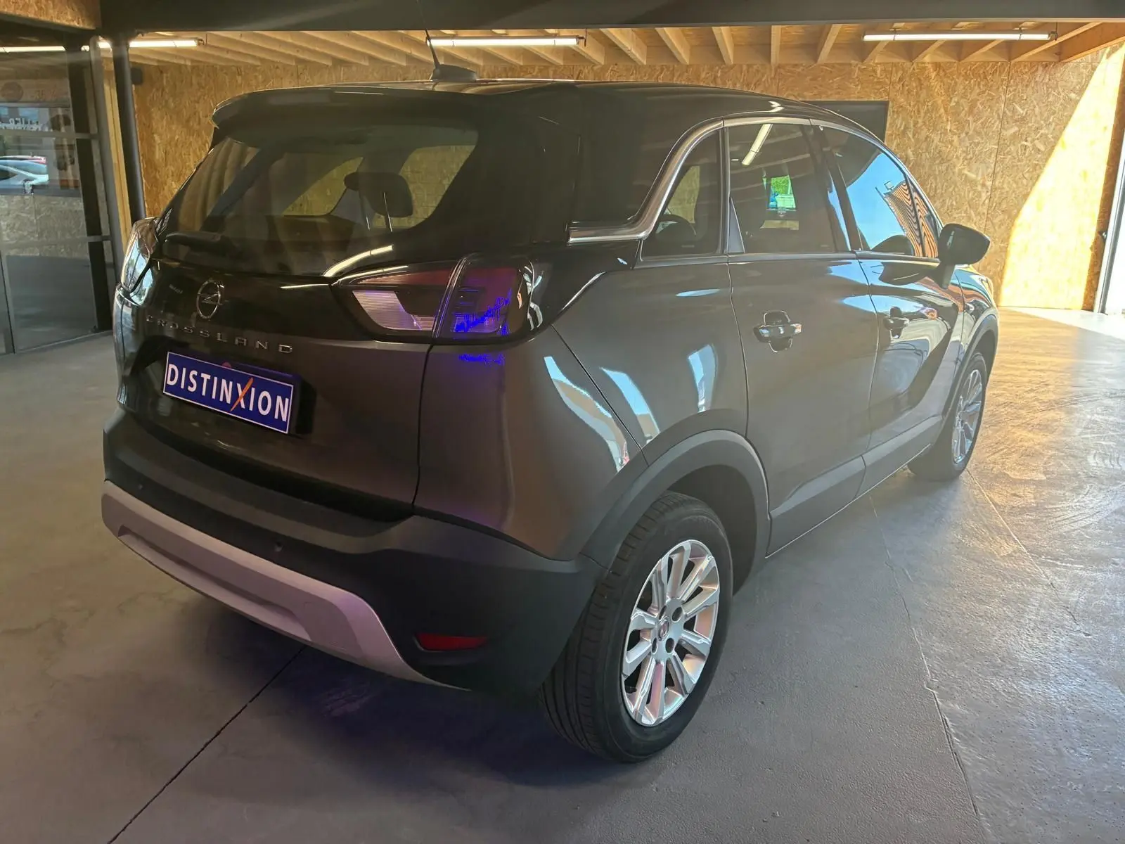 Vue 3/4 arrière droite d'un Opel Crossland gris 2021 avec jantes alliage et hayon fermé dans un garage.