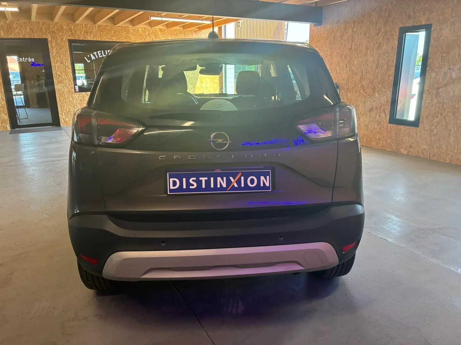 Vue arrière d'un Opel Crossland gris 2021 stationné en intérieur avec plaque Distinxion visible.