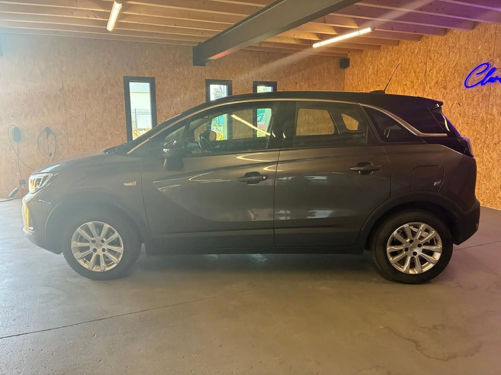 Vue de profil côté gauche d'un Opel Crossland gris 2021, version 1.2 Turbo 110 Elegance, en intérieur.
