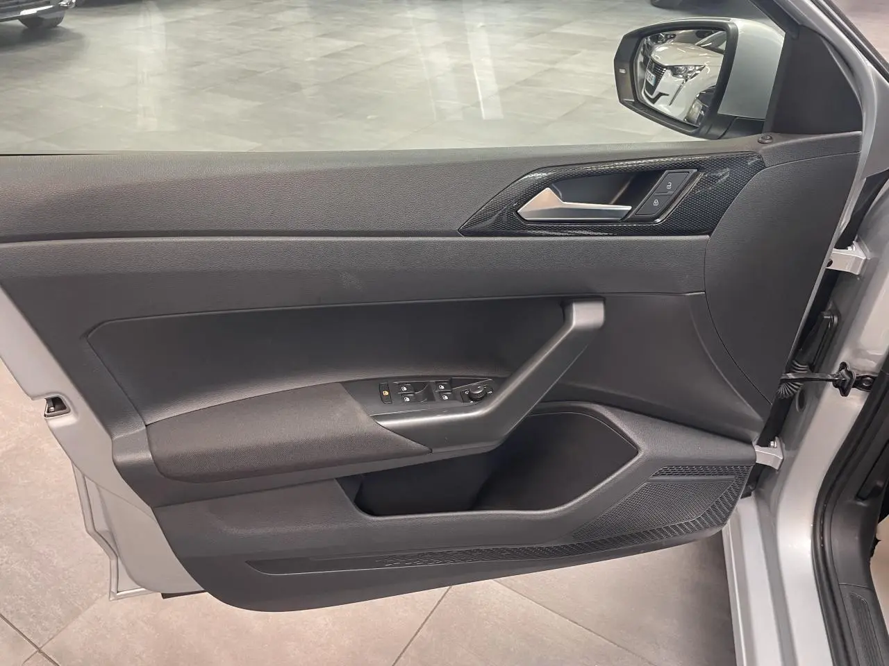 Vue de la porte avant droite ouverte d’une Volkswagen Polo gris clair, avec commandes électriques et insert décoratif noir.