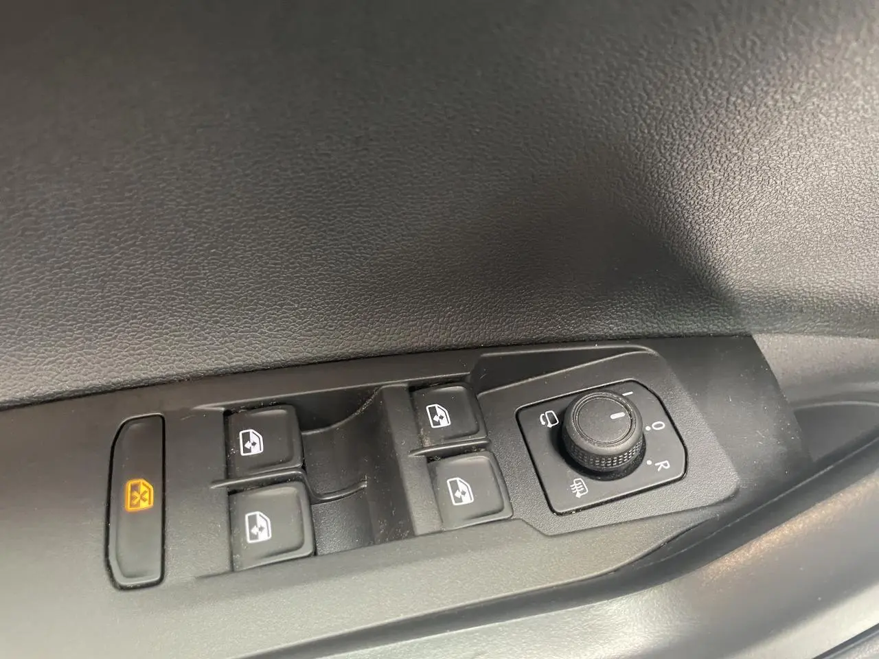 Gros plan sur les commandes de lève-vitres et réglage des rétroviseurs côté conducteur d’une Volkswagen Polo gris clair.