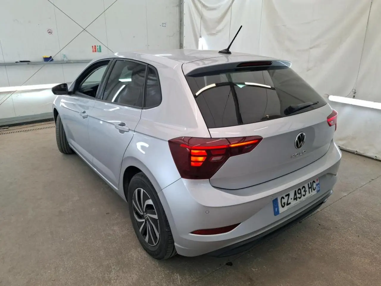 Volkswagen Polo gris clair vue 3/4 arrière droit avec feux arrière allumés dans un garage.