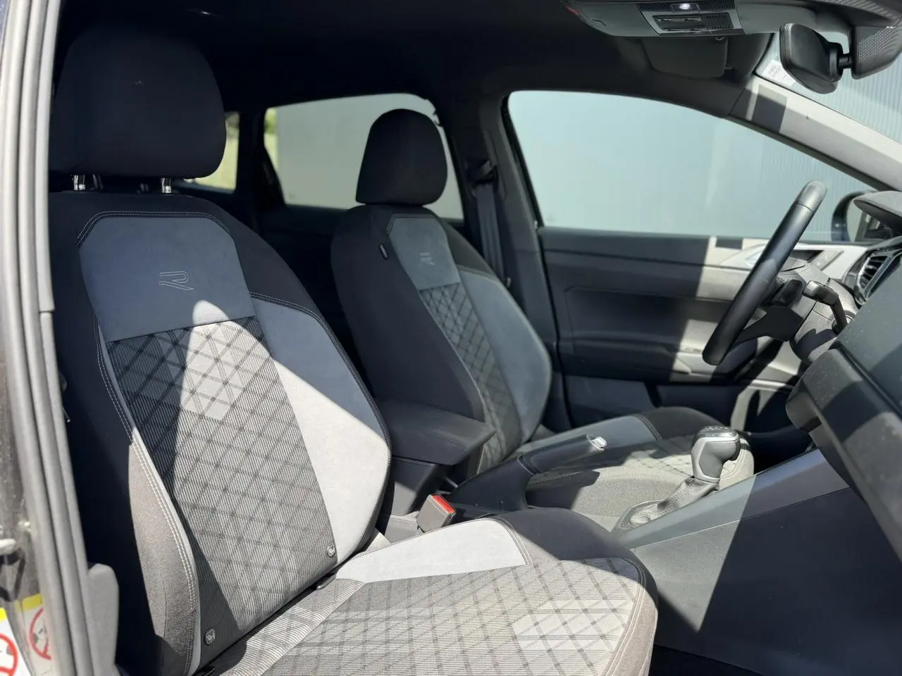 Vue intérieure côté gauche du Volkswagen Taigo TSI 116 DSG R-Line 2025, sièges sport tissu gris avec logo R-Line.