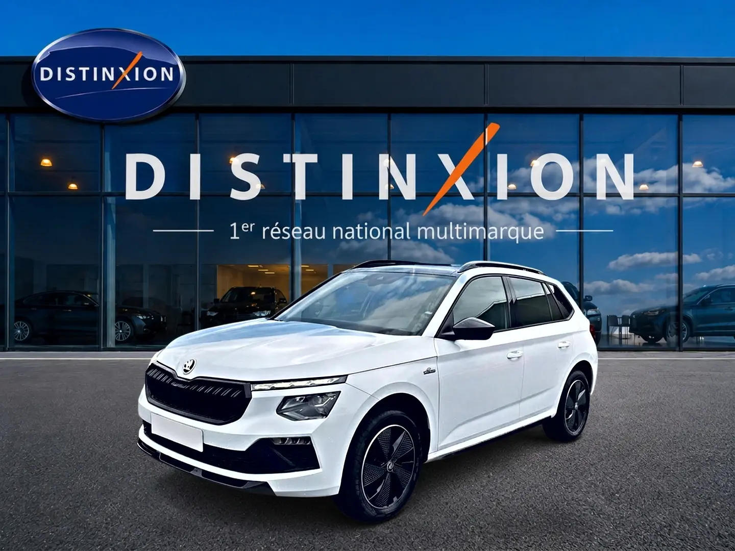 SKODA KAMIQ blanc nacré en 3/4 avant, avec jantes noires et toit panoramique visible devant une vitrine Distinxion.