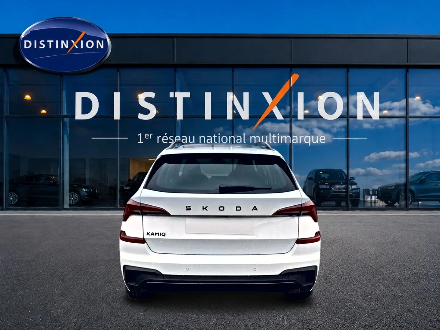 Vue arrière d'un Skoda Kamiq blanc nacré avec logo distinctif, garé devant une vitrine Distinxion.