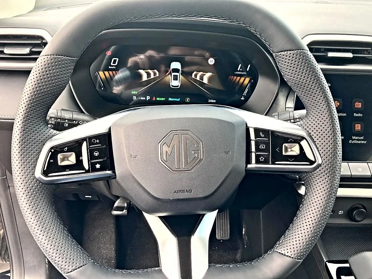 Vue rapprochée du volant noir perforé MG ZS 1.5 hybrid 197 luxury avec tableau de bord numérique en arrière-plan.