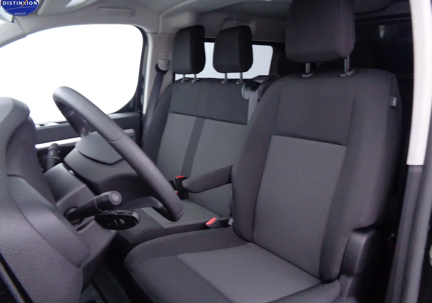 Vue intérieure côté conducteur du Peugeot Expert Long 2023, sièges tissu gris et noir, volant et tableau de bord visibles.