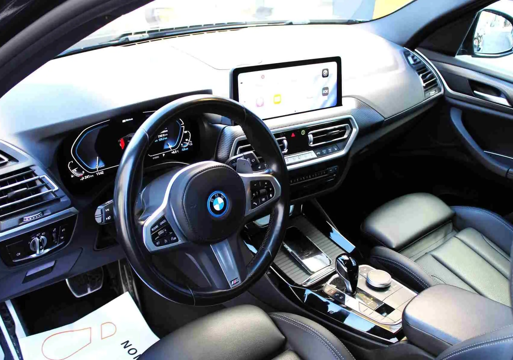 Intérieur du BMW X3 xDrive 30e 2023 vu côté conducteur, avec tableau de bord numérique et console centrale noire brillante.