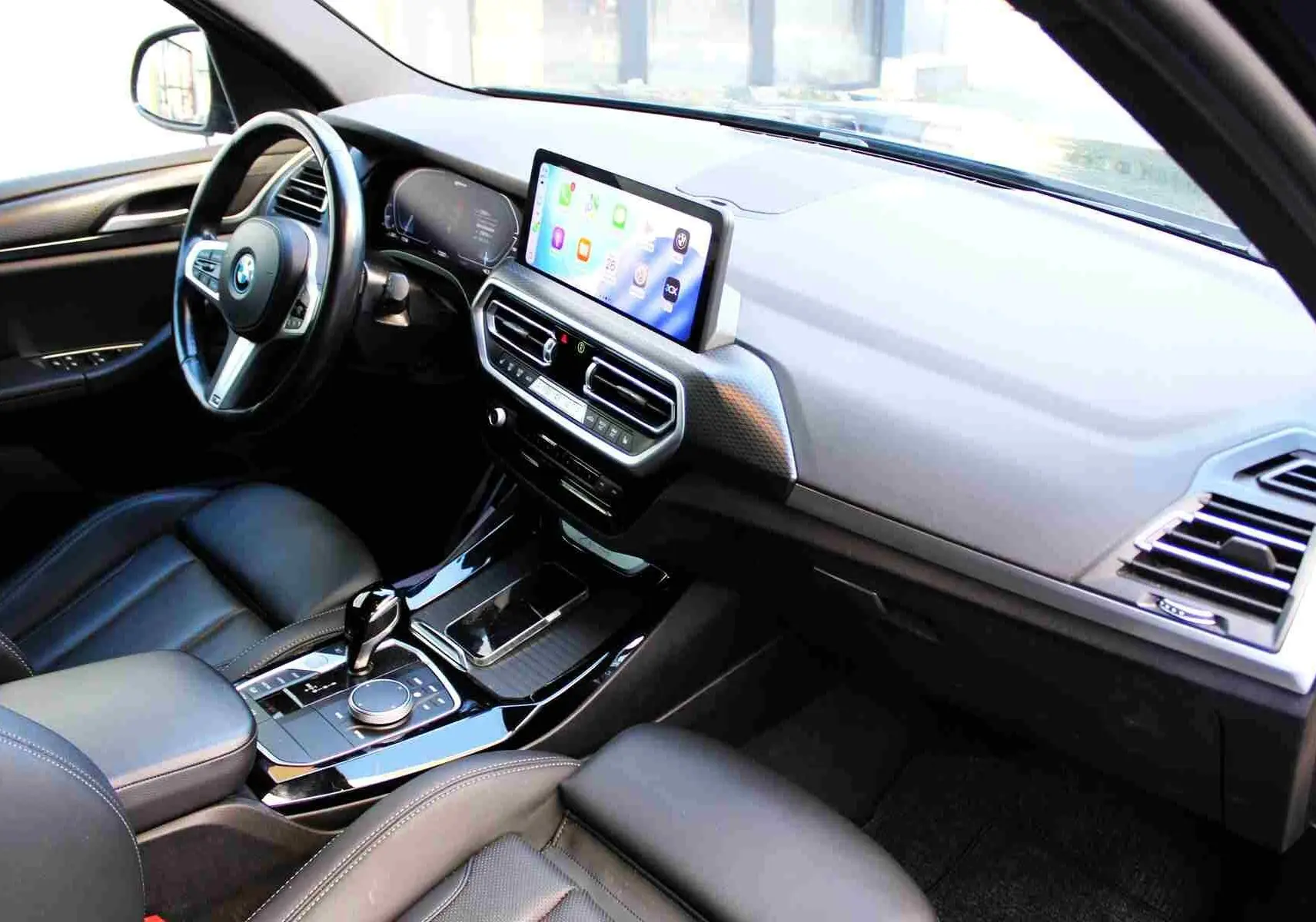 Intérieur BMW X3 xDrive 30e 2023, vue côté conducteur sur tableau de bord moderne avec écran tactile et cuir noir.