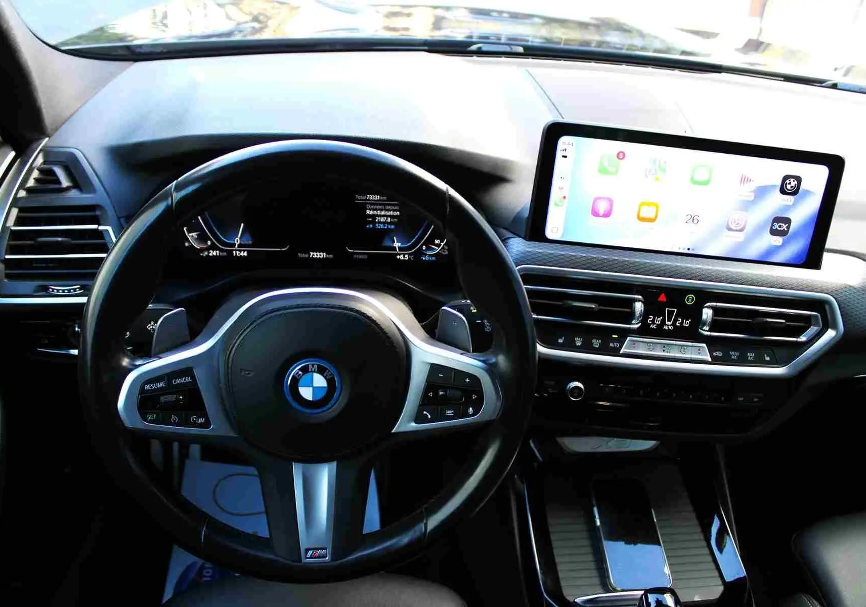 Vue intérieure du tableau de bord du BMW X3 xDrive 30e 2023, avec volant M Sport et écran tactile central lumineux.