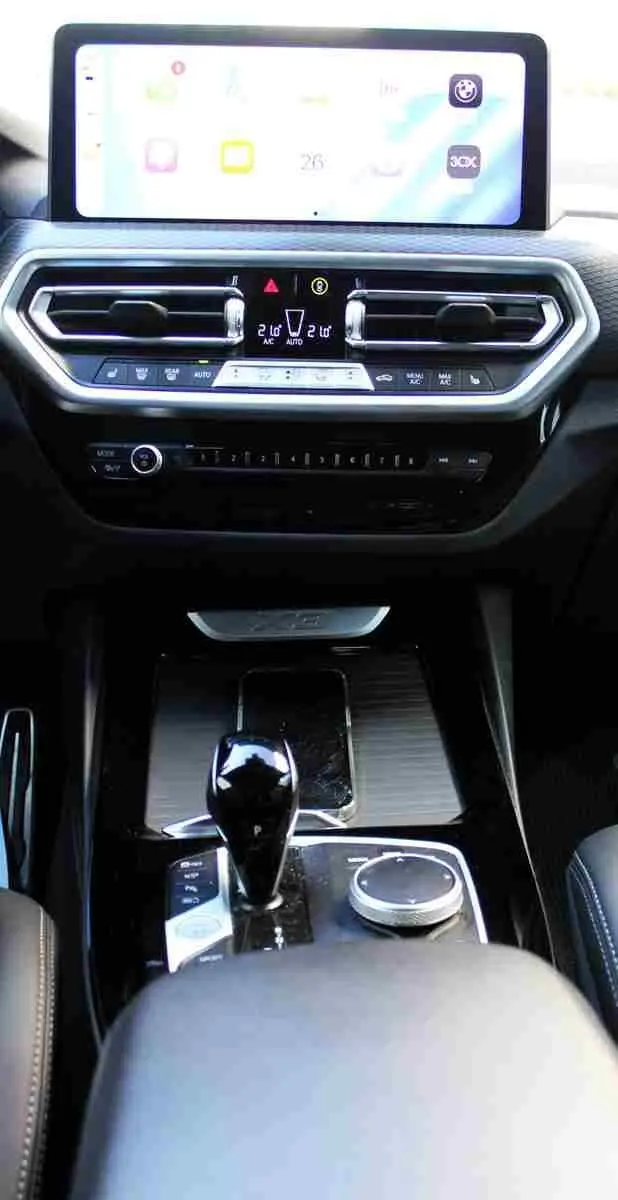 Vue intérieure centrée sur la console centrale et l'écran tactile du BMW X3 xDrive bleu métal 2023 hybride rechargeable.