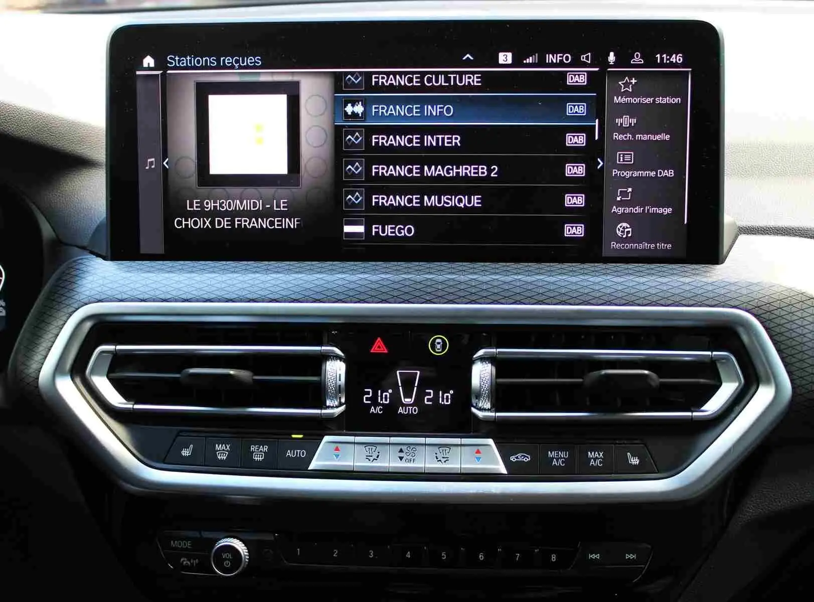 Tableau de bord du BMW X3 xDrive 30e 2023 avec écran tactile affichant les stations radio et commandes de climatisation modernes.