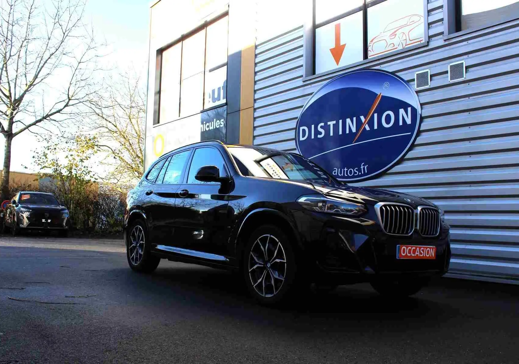BMW X3 xDrive 30e 2023 bleu métal vu en 3/4 avant droit devant un mur avec logo Distinxion.