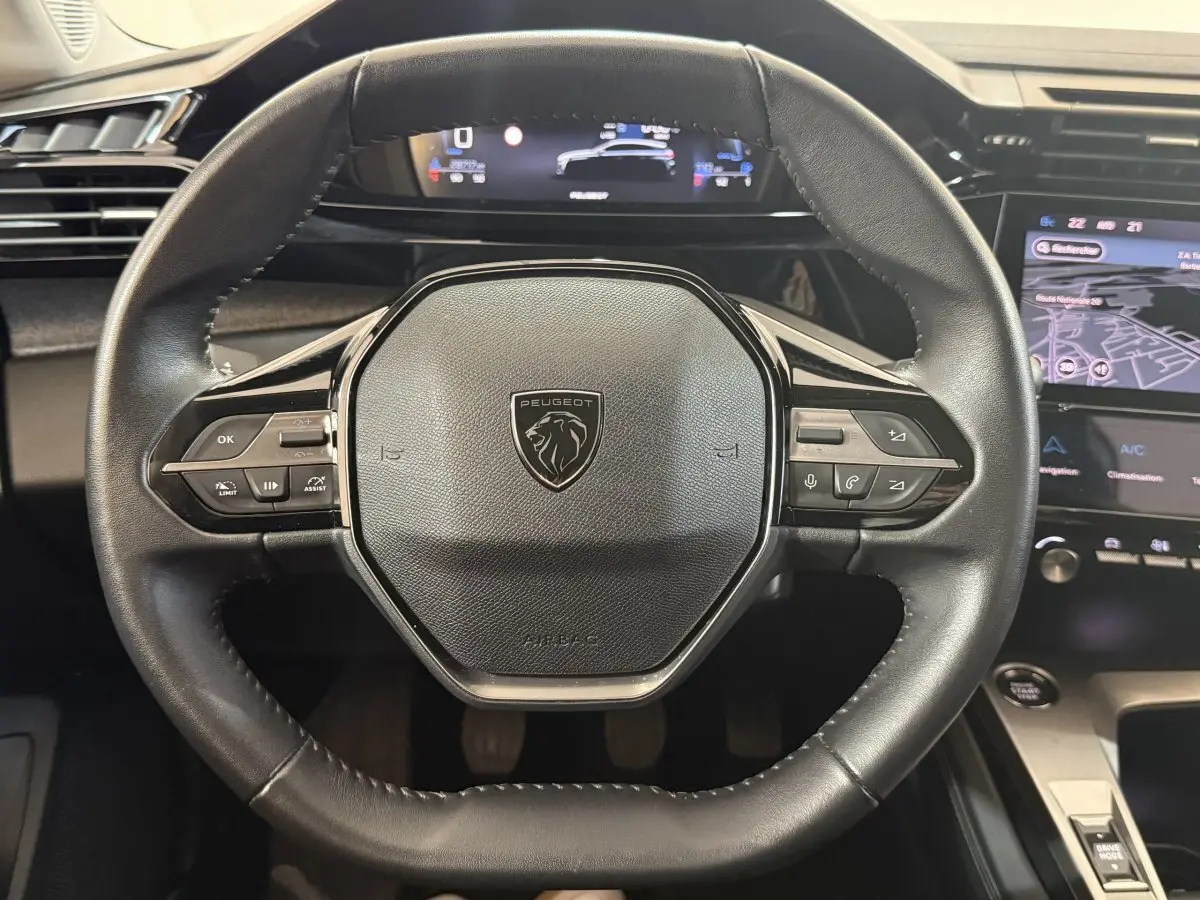 Vue rapprochée du volant cuir noir de la Peugeot 308 2023 avec commandes multifonctions et tableau de bord numérique.