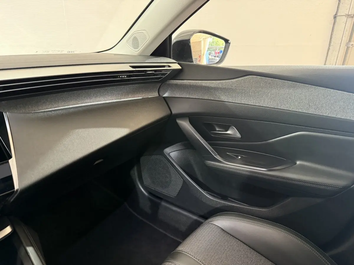Intérieur côté passager de la Peugeot 308 bleu 2023, montrant la porte, le tableau de bord et siège en cuir noir.