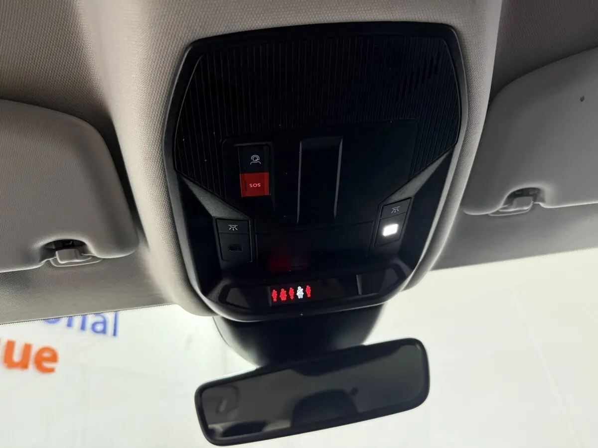 Vue intérieure en plongée du panneau de commandes au plafond noir avec bouton SOS rouge et éclairage dans une Peugeot 308 bleu 2023.