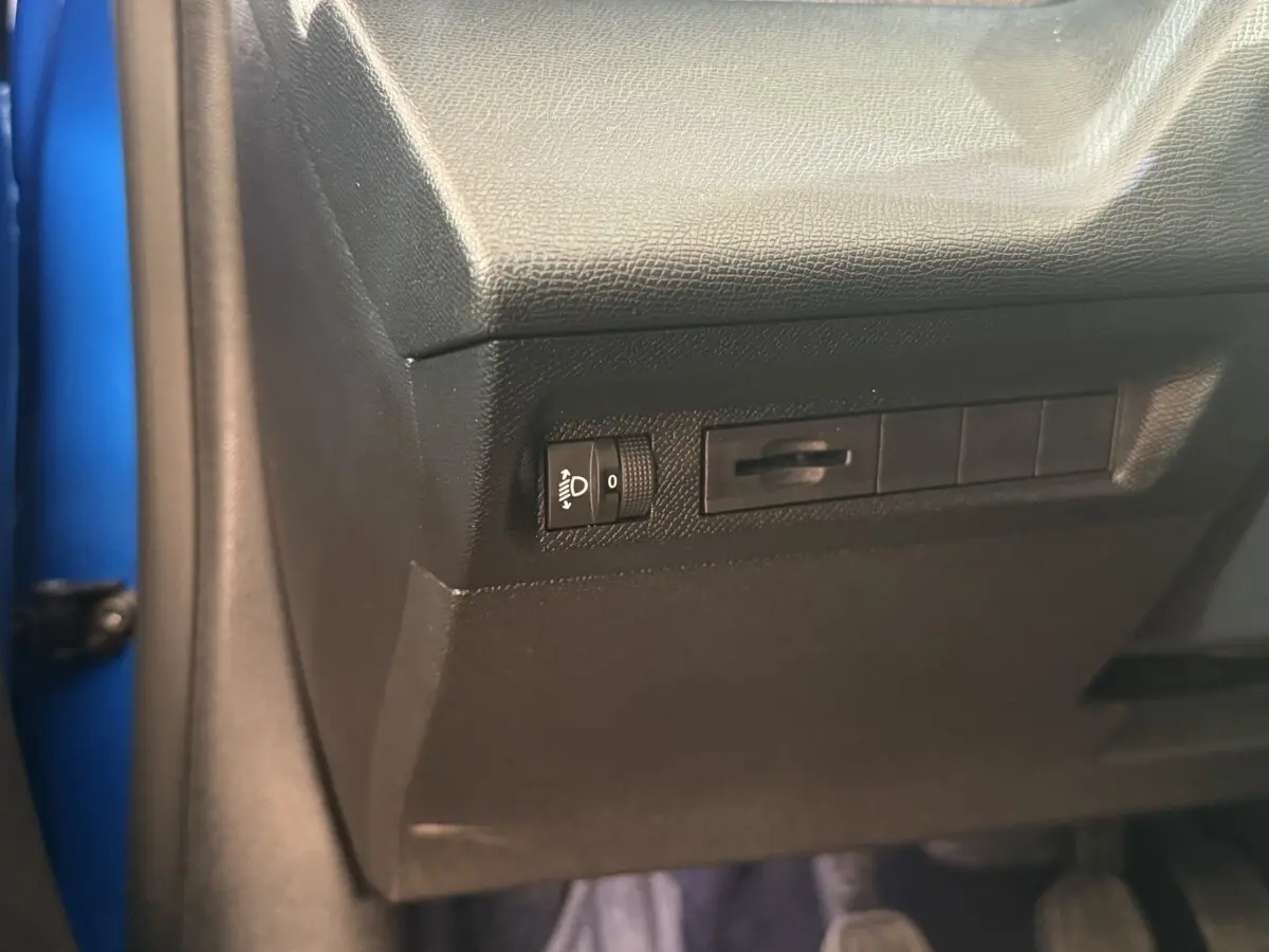 Détail du panneau de réglage des phares sur la partie inférieure gauche du tableau de bord d'une Peugeot 308 bleu 2023.