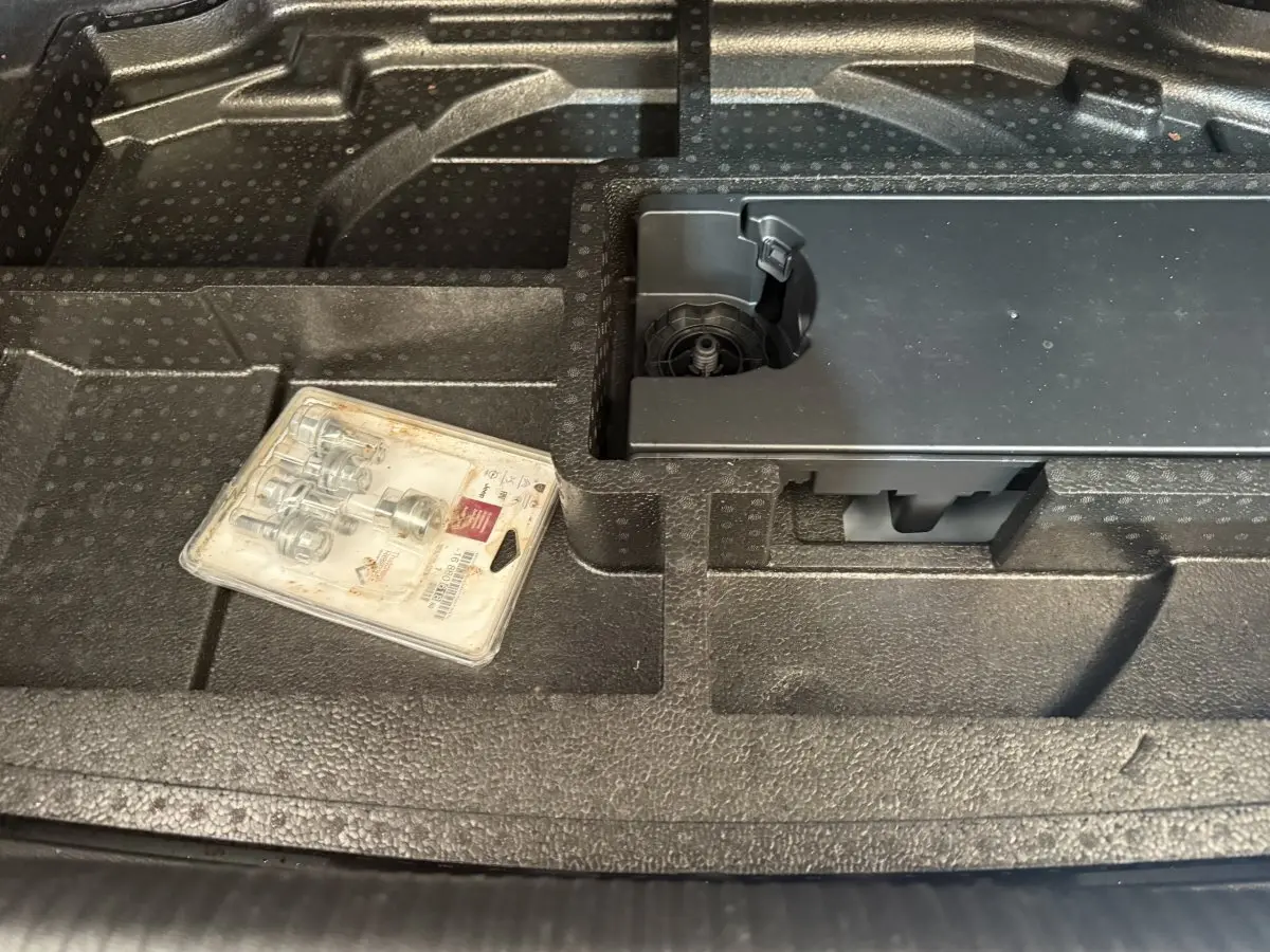 Gros plan sur le rangement en mousse noir dans le coffre d'une Peugeot 308 bleu, avec un kit de visserie posé.
