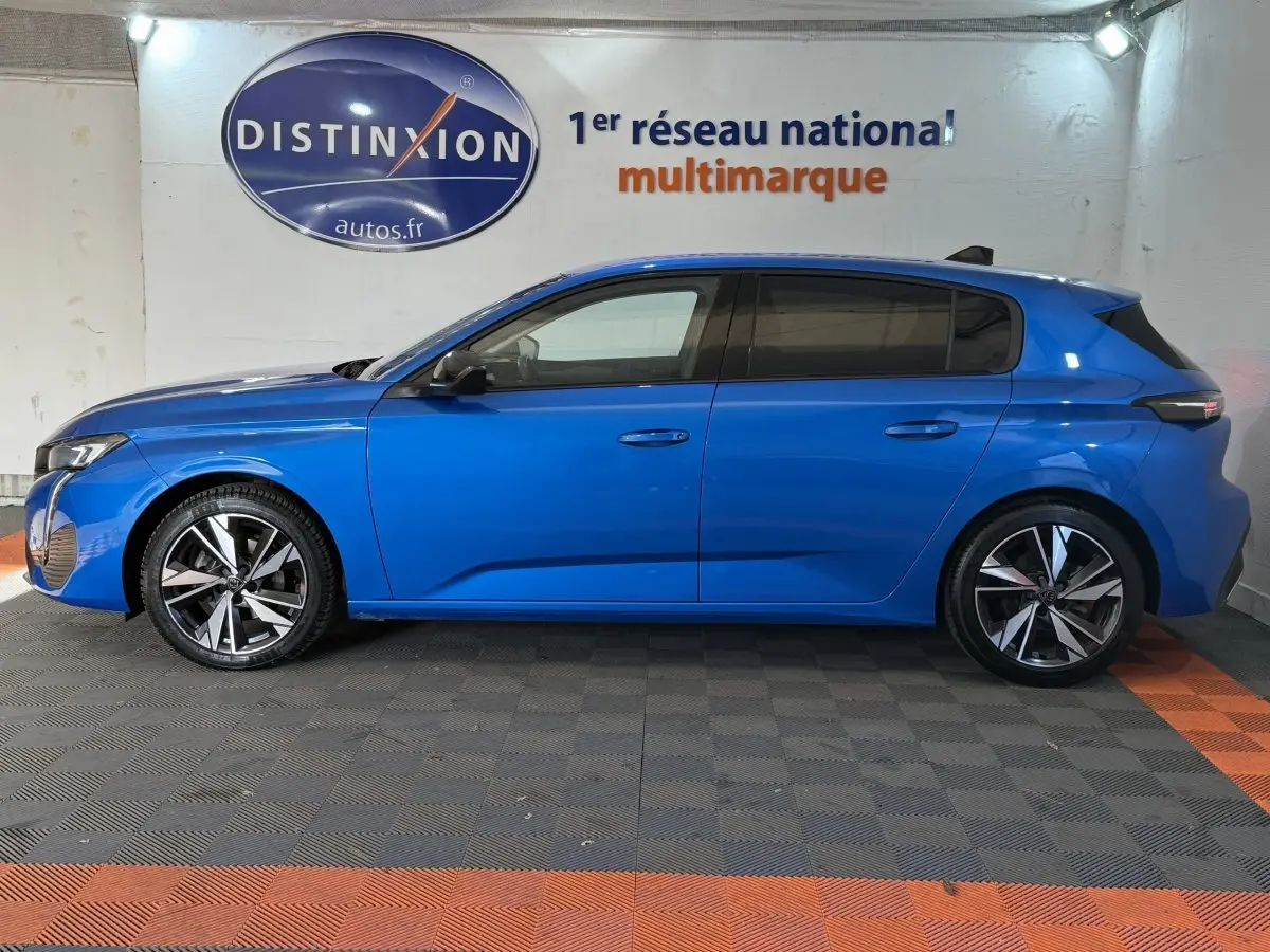 Profil côté gauche d'une Peugeot 308 bleu 2023 avec jantes alliage et vitres teintées, en intérieur showroom.