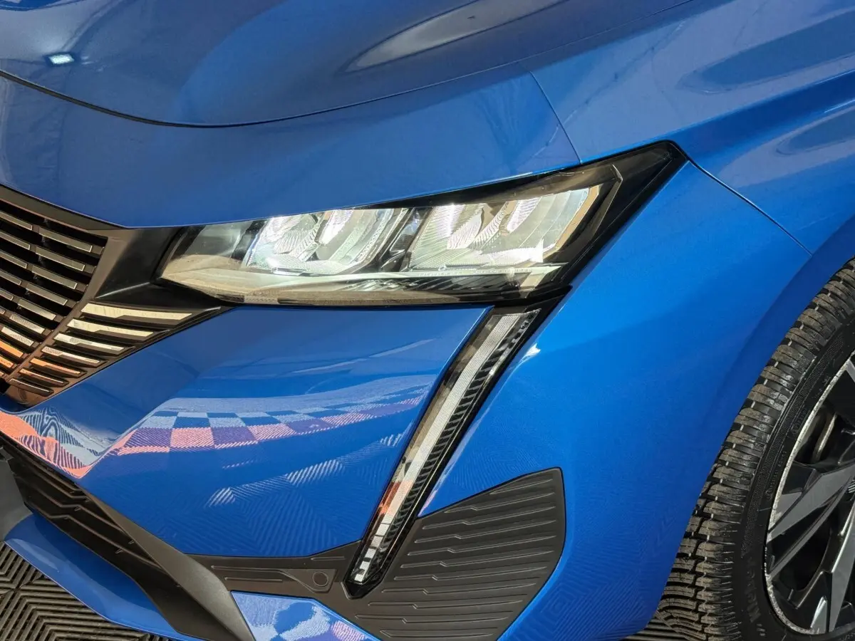 Gros plan sur l'avant droit bleu vif de la Peugeot 308 2023, mettant en valeur le phare LED et la calandre distinctive.