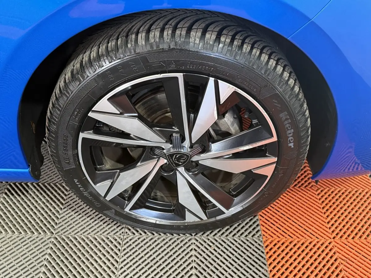 Gros plan sur la roue avant gauche de la Peugeot 308 bleu, avec jante alliage noire et argentée au design moderne.