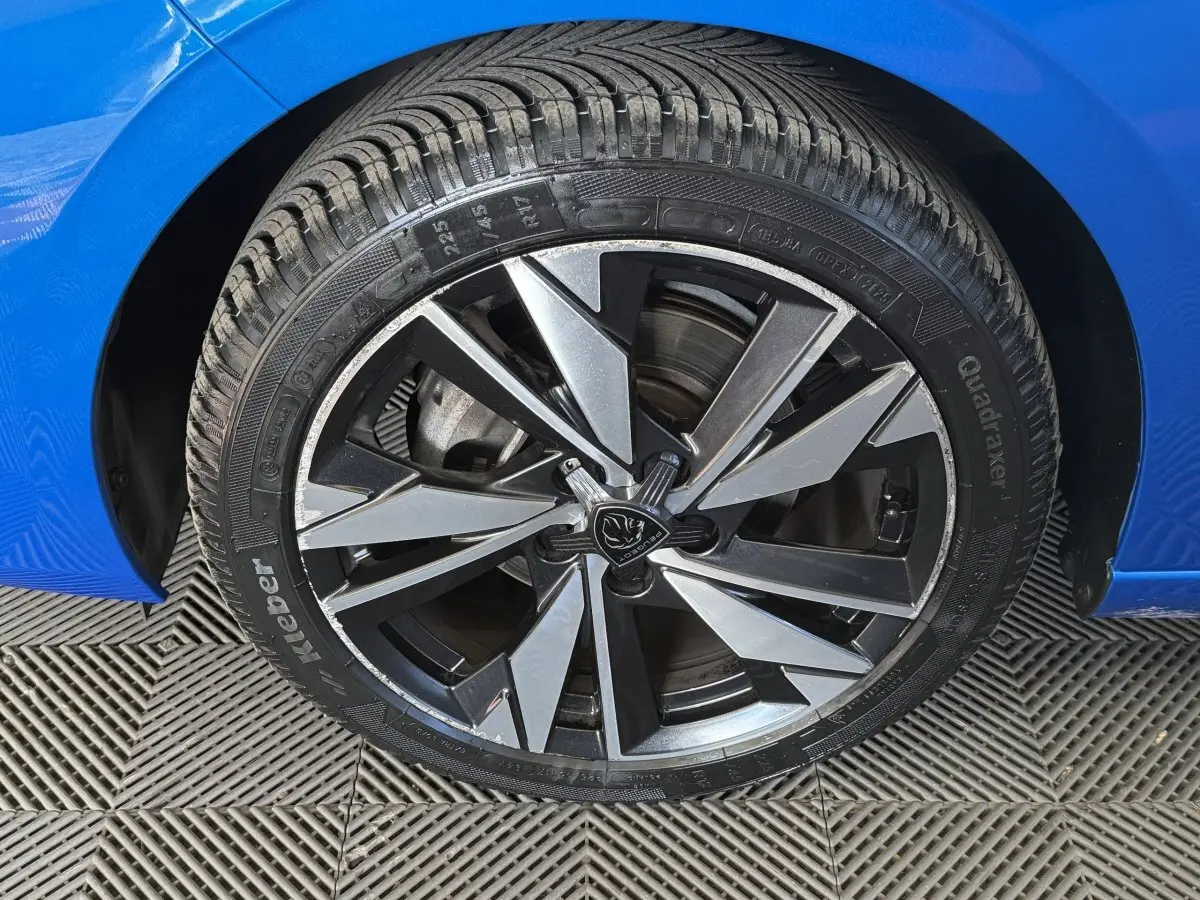 Gros plan sur la roue avant droite d’une Peugeot 308 bleu, avec jante alliage noire et argentée au design moderne.