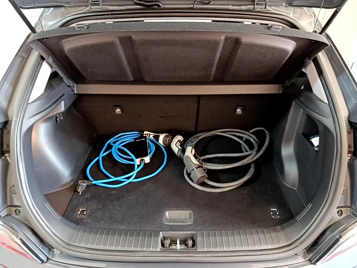 Coffre ouvert d'une Hyundai Kona électrique gris foncé avec câbles de recharge visibles à l'intérieur.