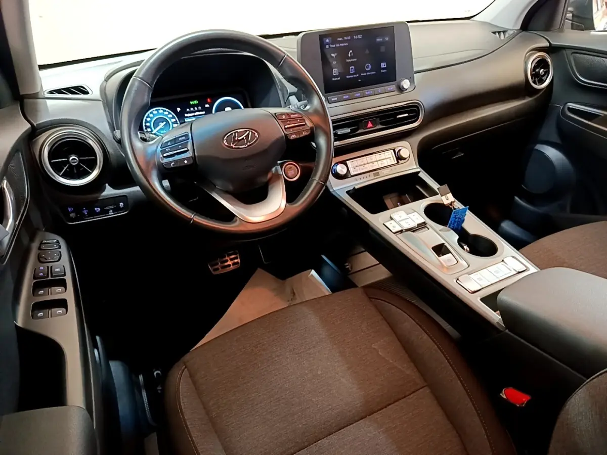 Vue intérieure avant du Hyundai Kona électrique 2021, volant cuir multifonctions et écran tactile central visible.