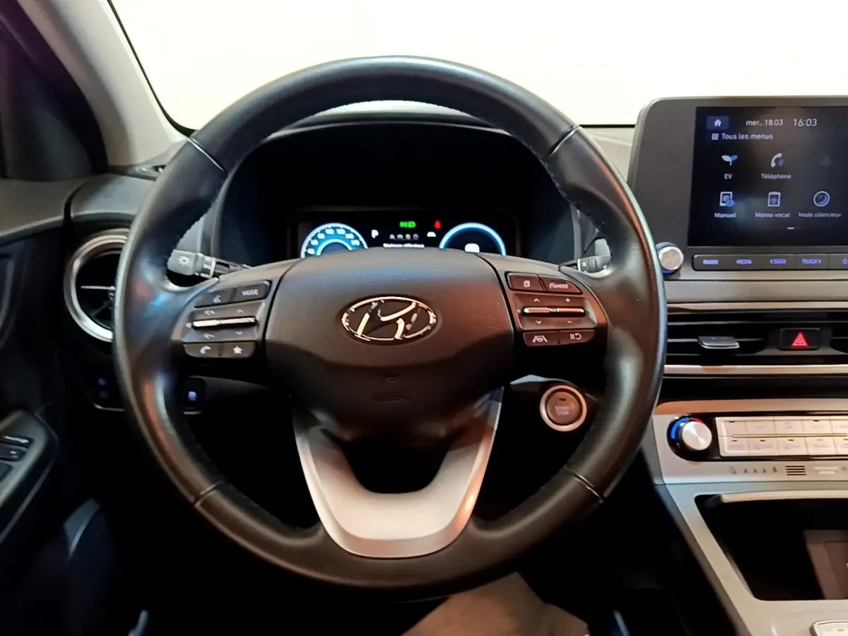 Vue intérieure centrée sur le volant cuir multifonctions noir d’une Hyundai Kona électrique avec tableau de bord digital et écran tactile.