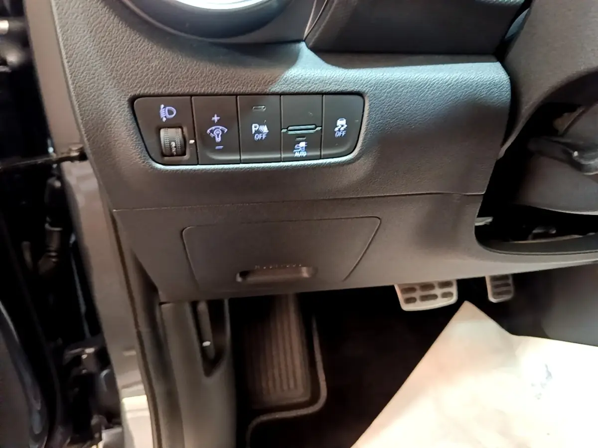 Vue rapprochée côté conducteur du tableau de bord noir avec commandes d’éclairage et aides à la conduite du Hyundai Kona électrique.